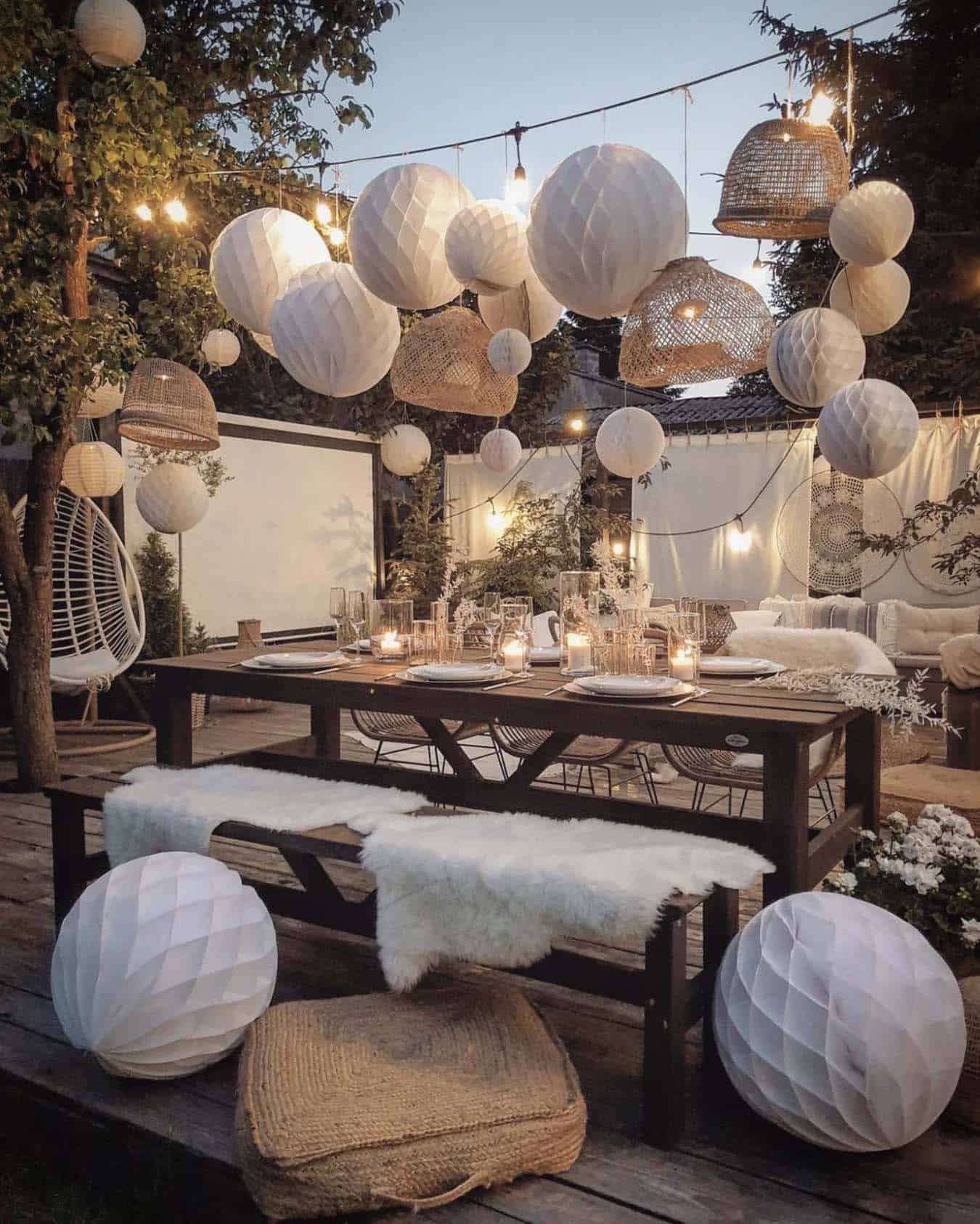 outdoor dining table with privacy screens and a movie projector along with string lights and hanging lamps