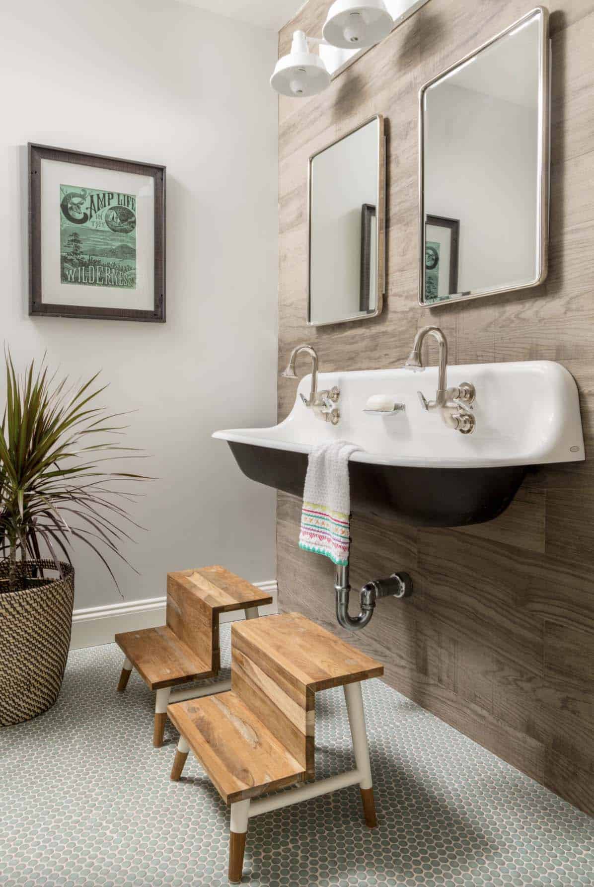 farmhouse kids bathroom with a trough sink and wood accent wall and penny round tile on the floor