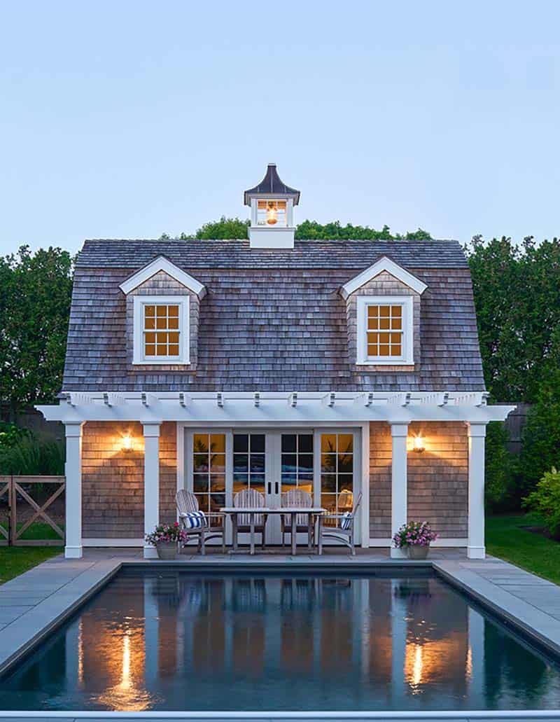 shingle style home exterior with a pool and pool house at dusk