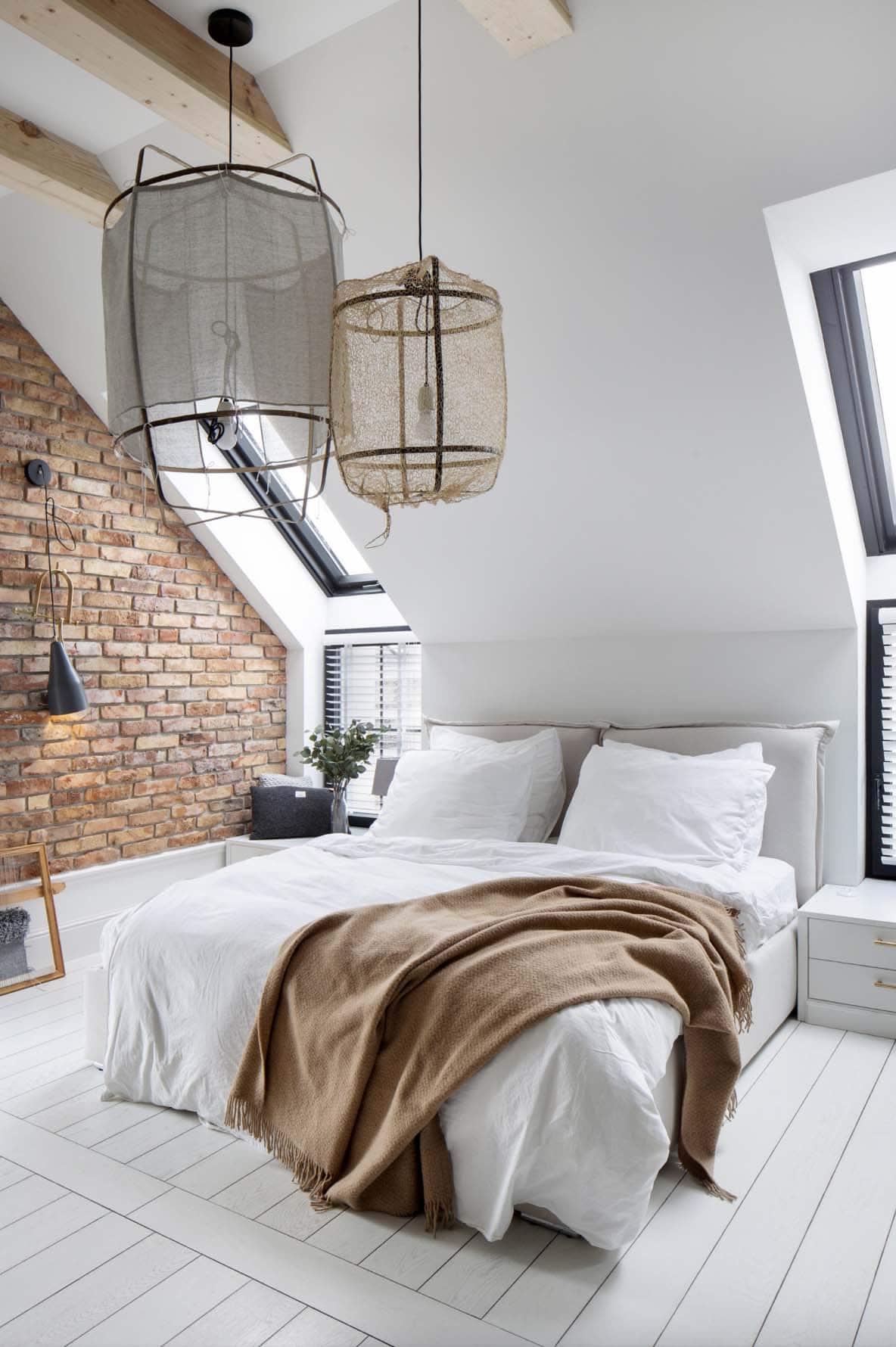 Scandinavian style bedroom with a sloped ceiling, large light fixtures and a brick accent wall