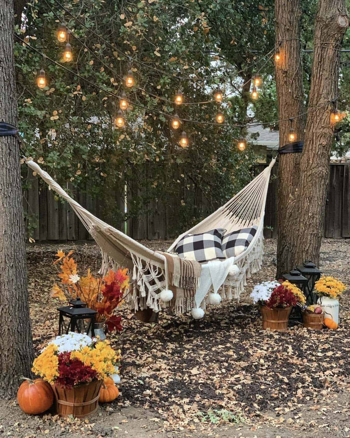 outdoor hammock decorated with fall pillows, throws, pumpkins and mums