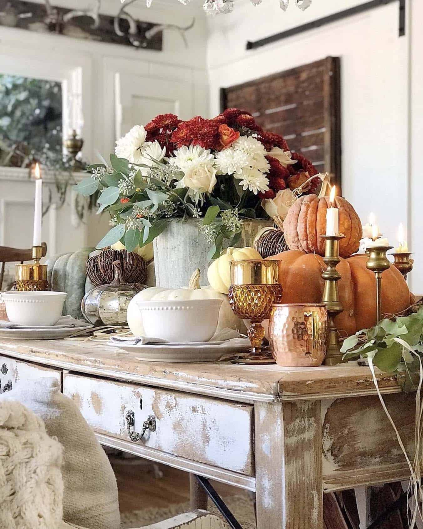 autumnal tablescape with flowers and stacked orange pumpkins and copper mugs 