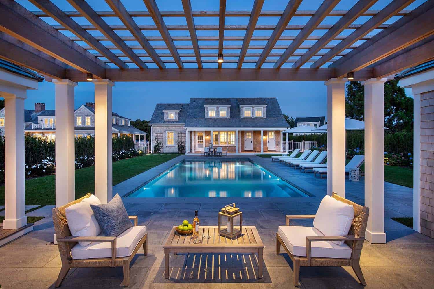coastal style trellis and outdoor furniture with a view of the swimming pool at dusk