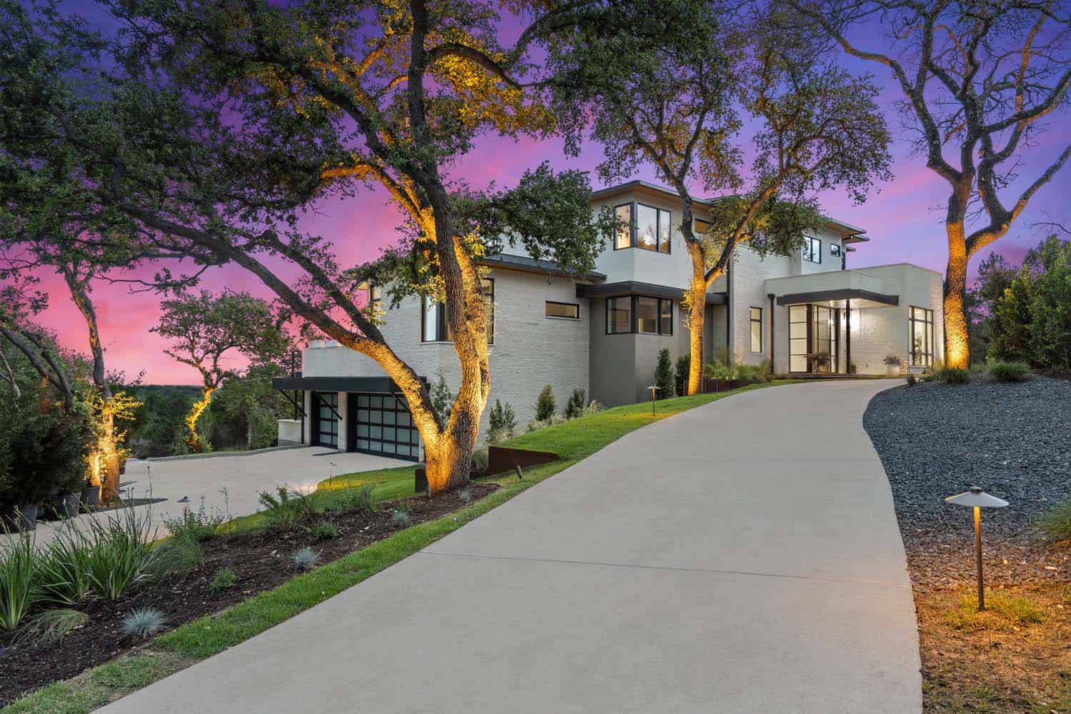 modern hillside home exterior with a driveway view at dusk