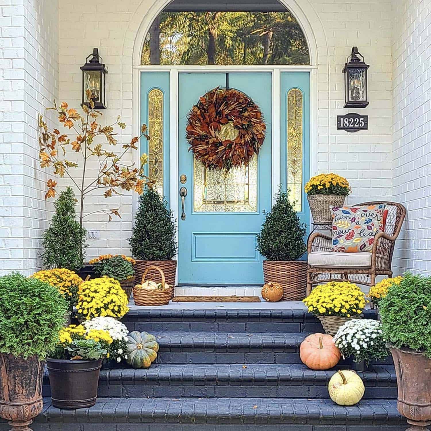 front porch with a blue door and fall flowers mixed with pumpkins