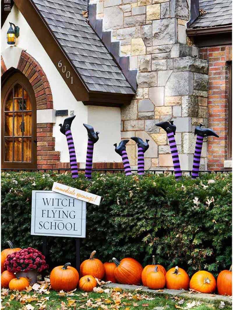 witch flying school sign with witches legs in the bushes in front of a house