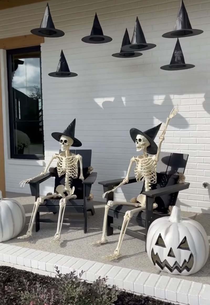 skeletons on the front porch with lighted pumpkins and floating witches hats