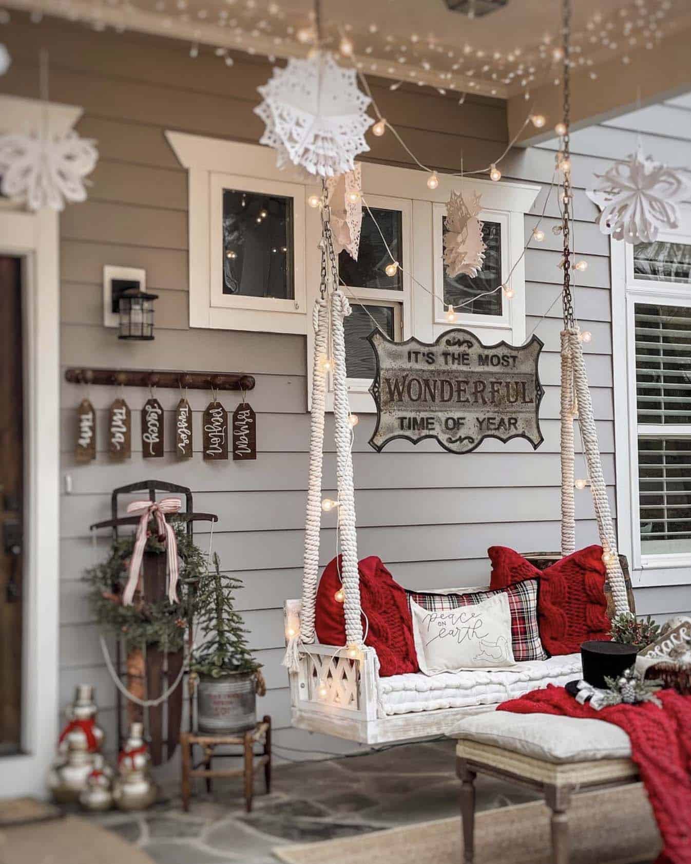 Christmas cozy porch swing with red pillows, a wreath, and a sign