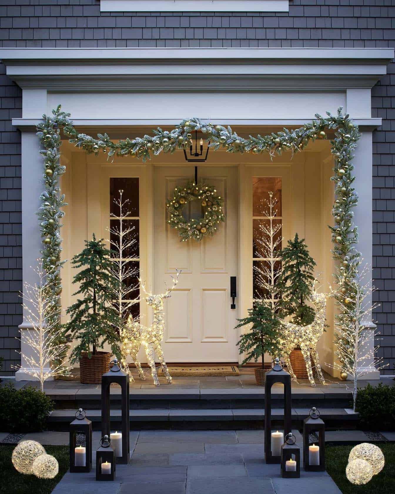 christmas decorated front porch with modern garland, trees, a door wreath and lighted reindeer