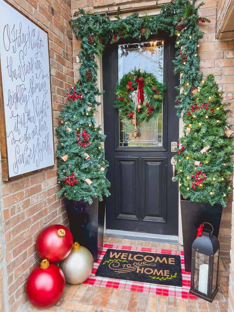 christmas decorated front porch with over-sized ornaments, trees, garland and a door wreath
