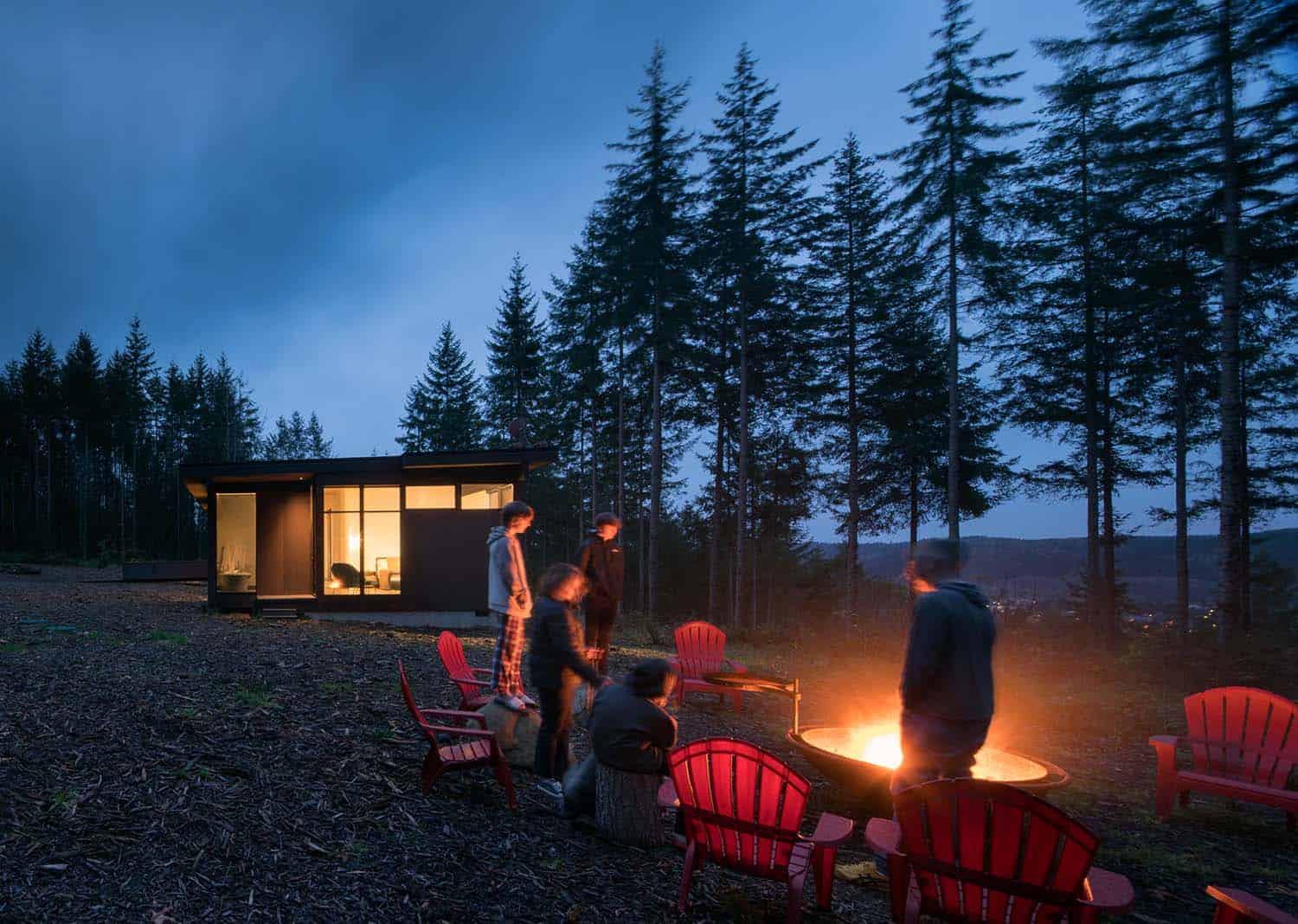 modern steel forest house exterior with a fire pit at dusk