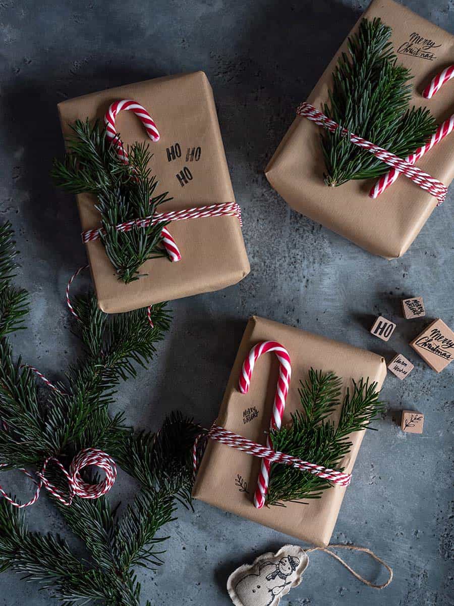 brown Kraft paper christmas gifts with candy canes, pine sprigs, twine and stamps