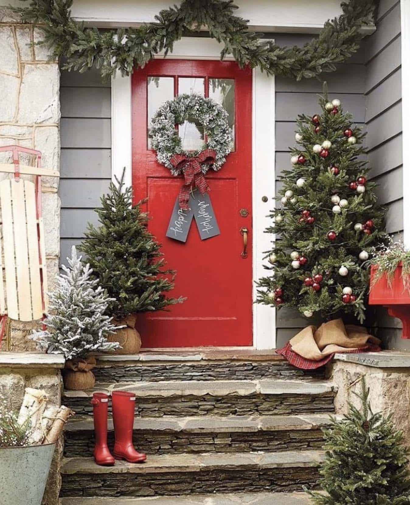 christmas decorated front porch with a red door and lighted trees and red rain boots