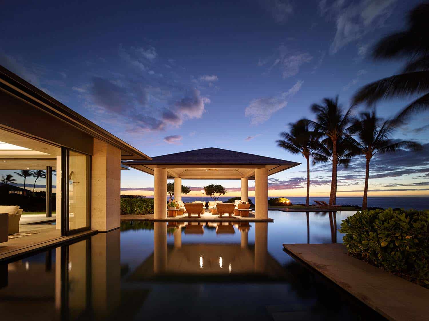 modern coastal style outdoor dining pavilion and swimming pool at dusk