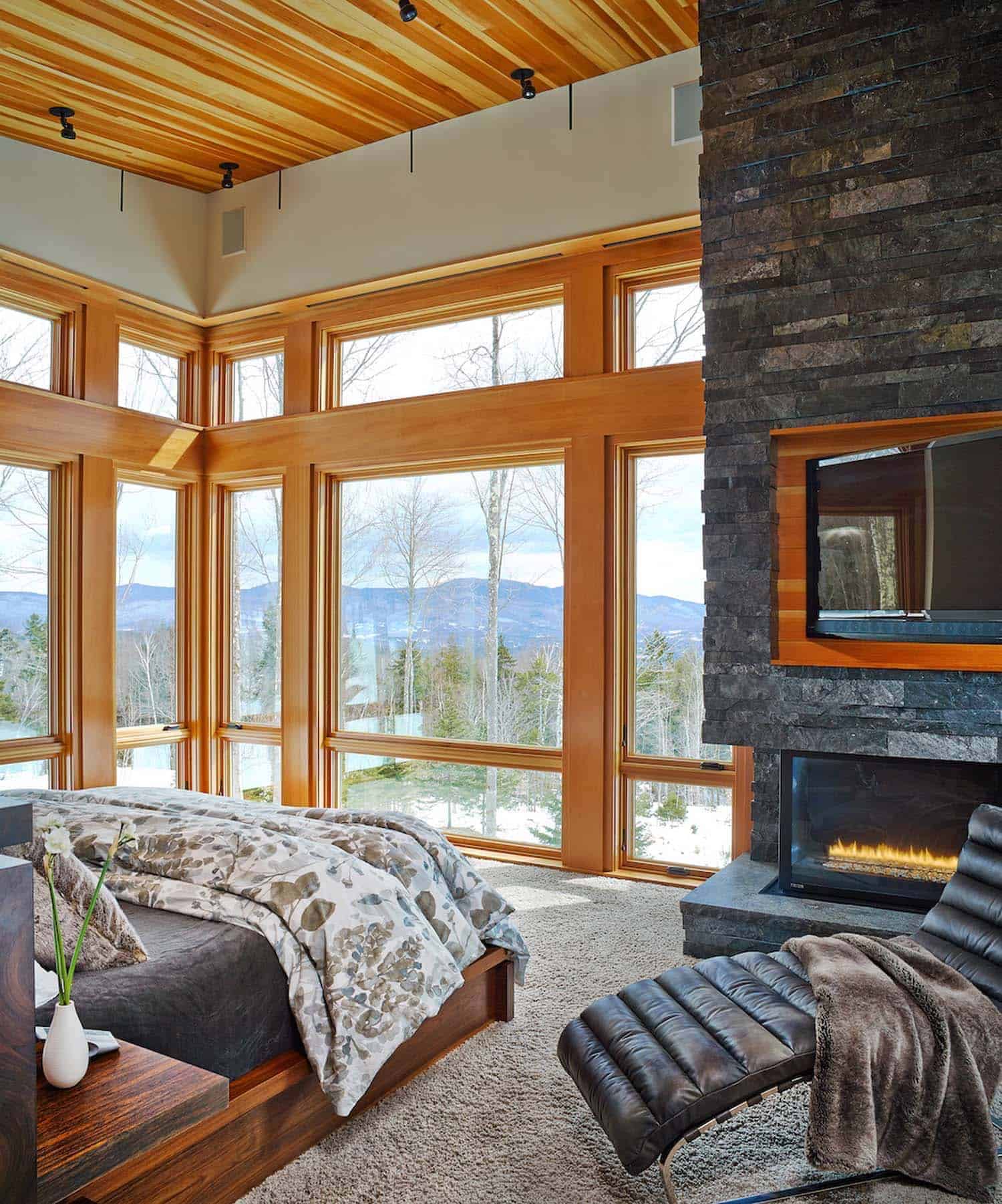 contemporary mountain style bedroom with a fireplace and large windows
