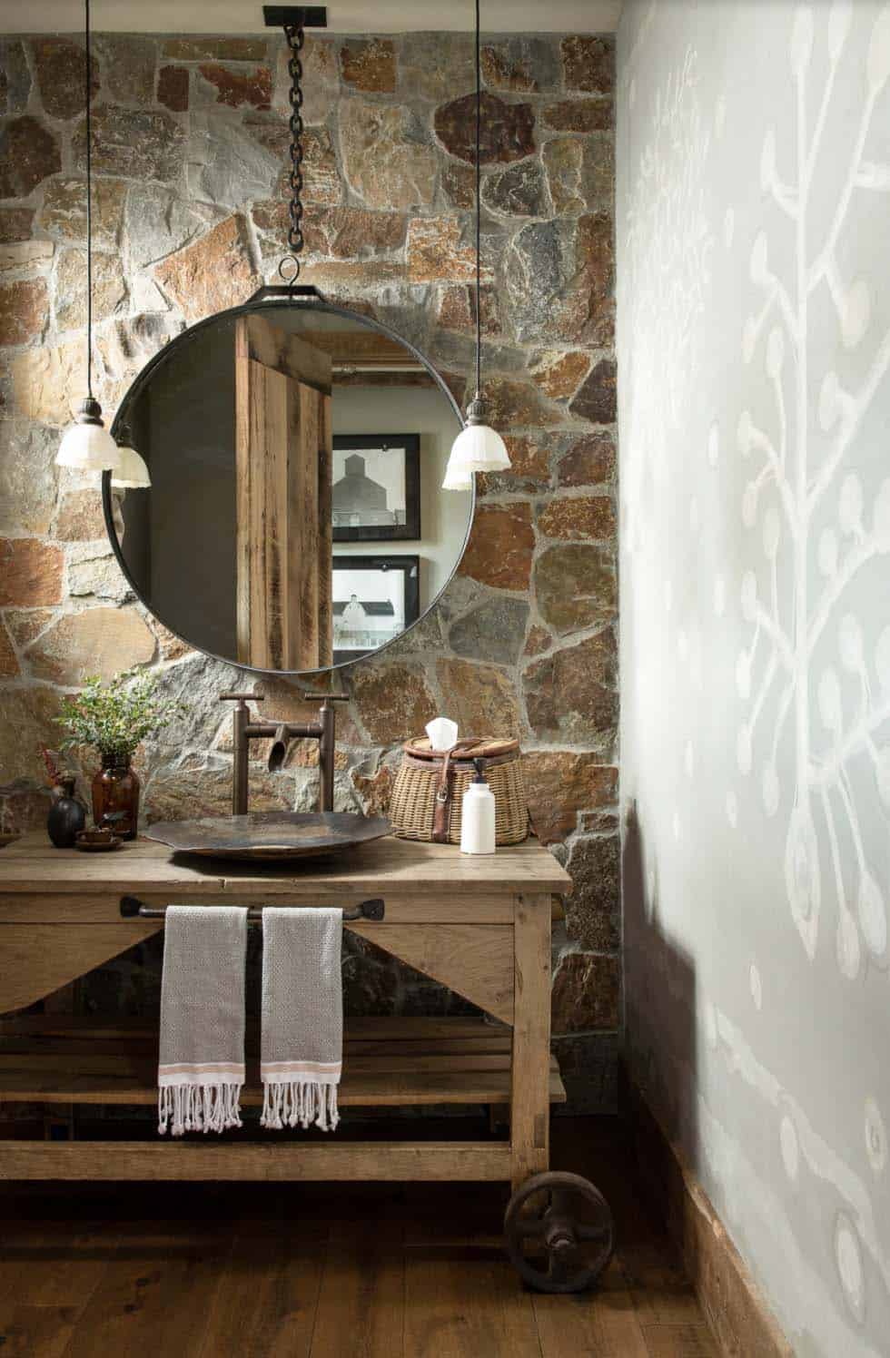 rustic powder room with a stone accent wall and large round mirror