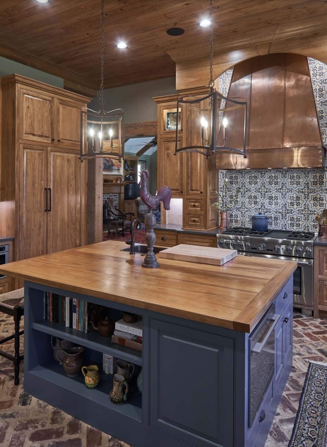 rustic kitchen with a blue painted island and wood countertop and custom copper hood