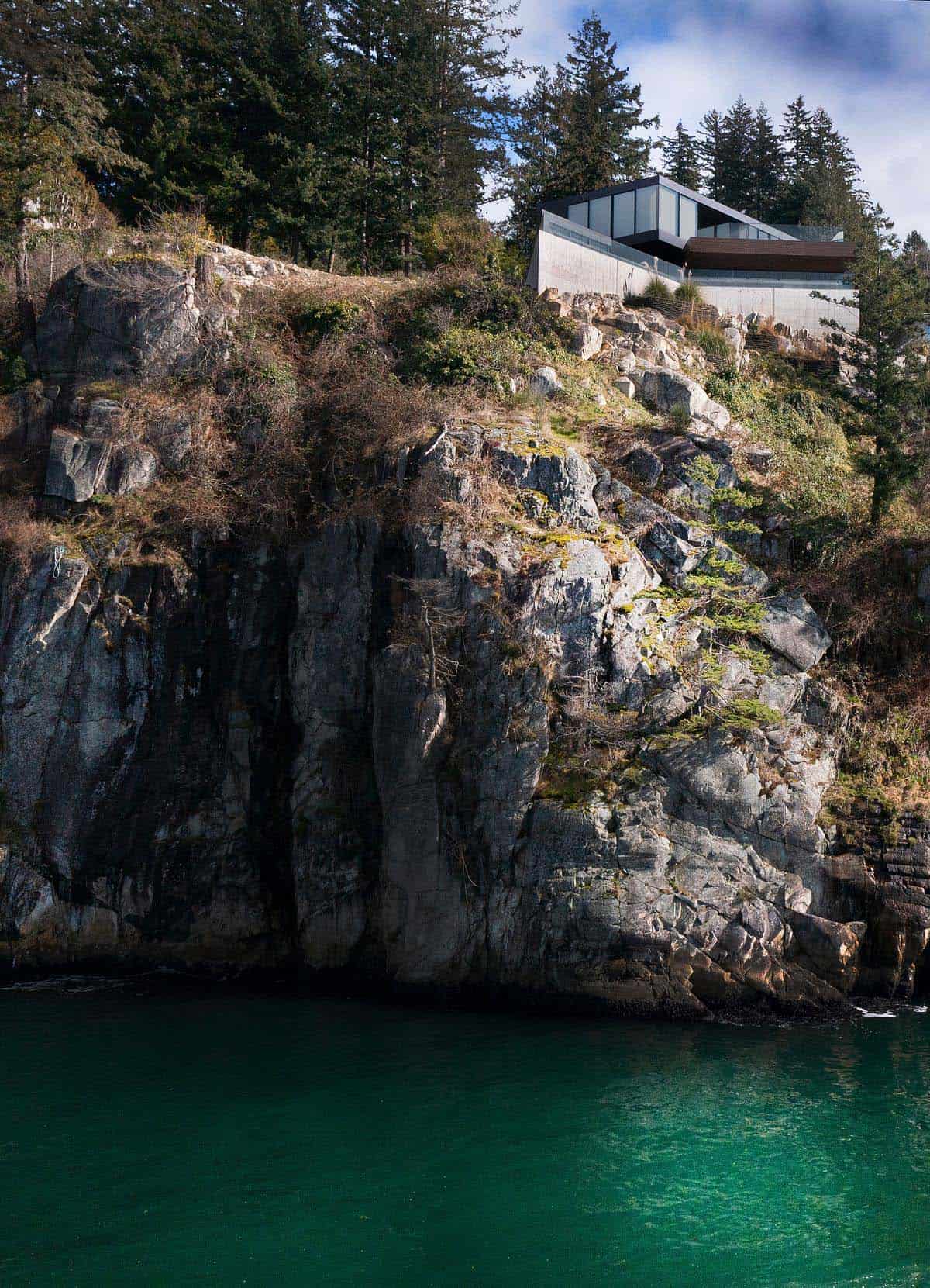view from the shoreline of the modern house perched on a granite rock