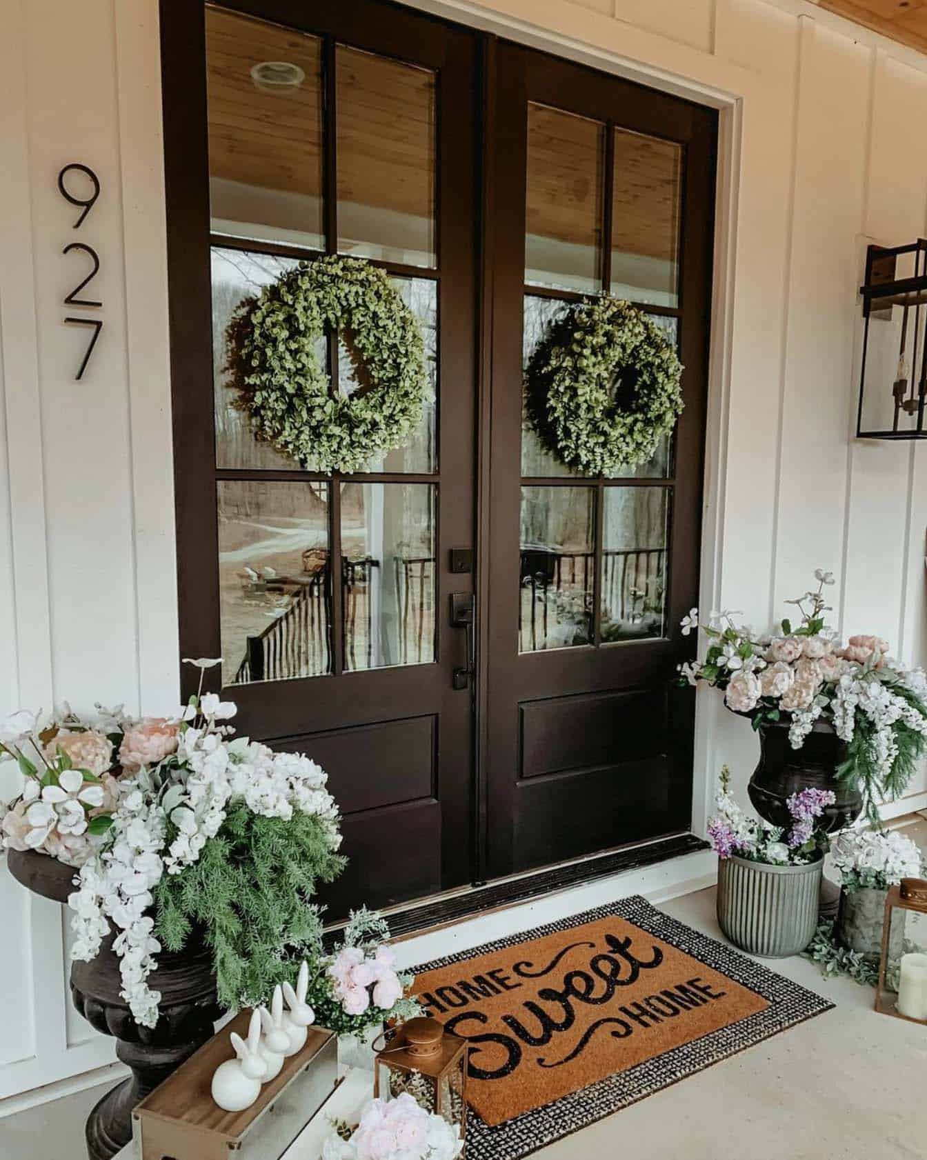 front porch decorated for spring with faux flowers, wreaths and a doormat
