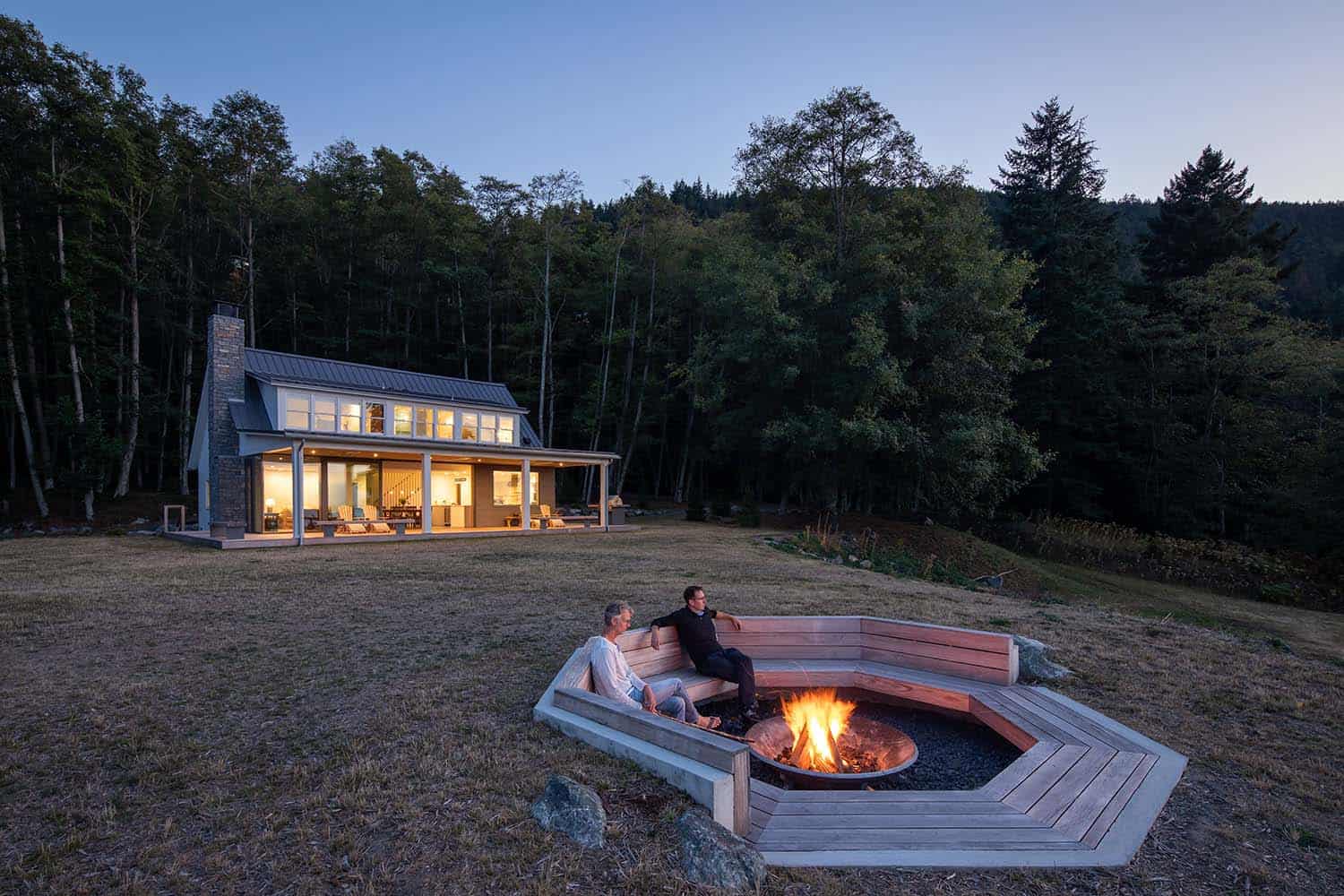 contemporary waterfront farmhouse exterior with a fire pit at dusk