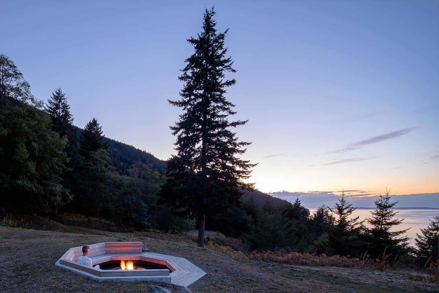 contemporary waterfront farmhouse exterior with a fire pit at dusk