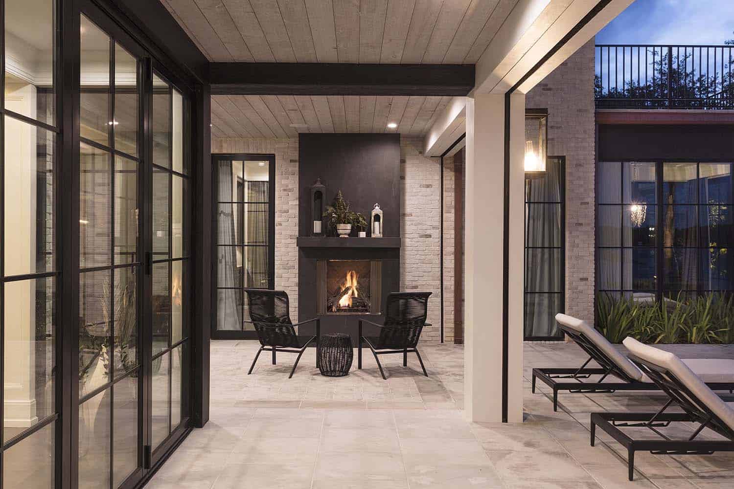 transitional style lake house covered patio with a fireplace at dusk