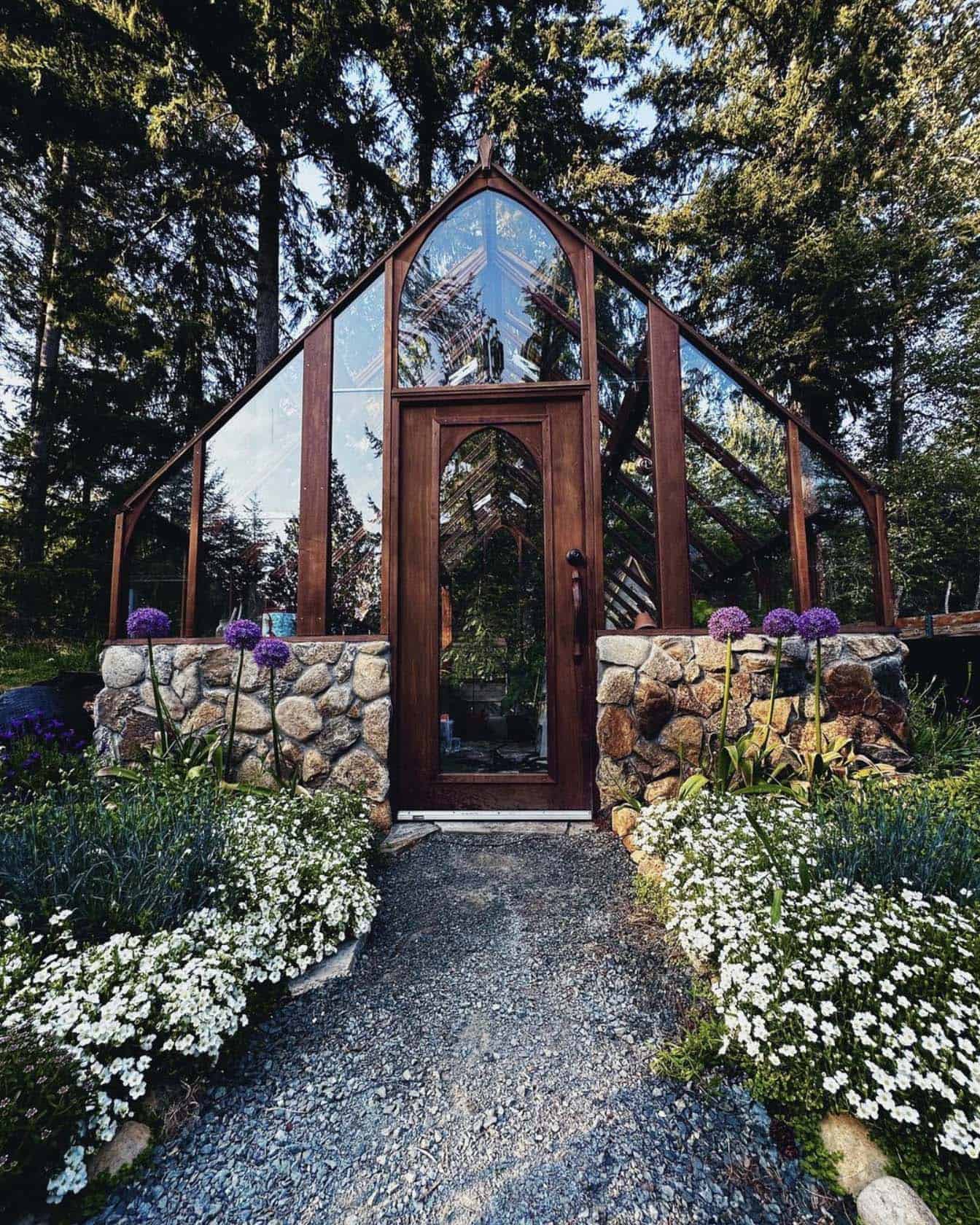 wood and glass greenhouse surrounded by flowers