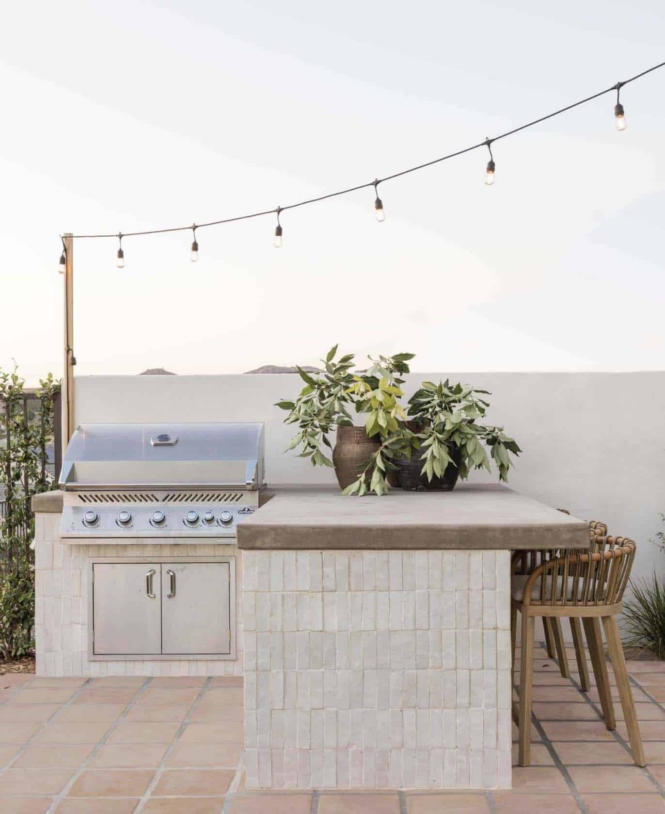 beach style patio with a bbq and bar top with counter stools and overhead string lights