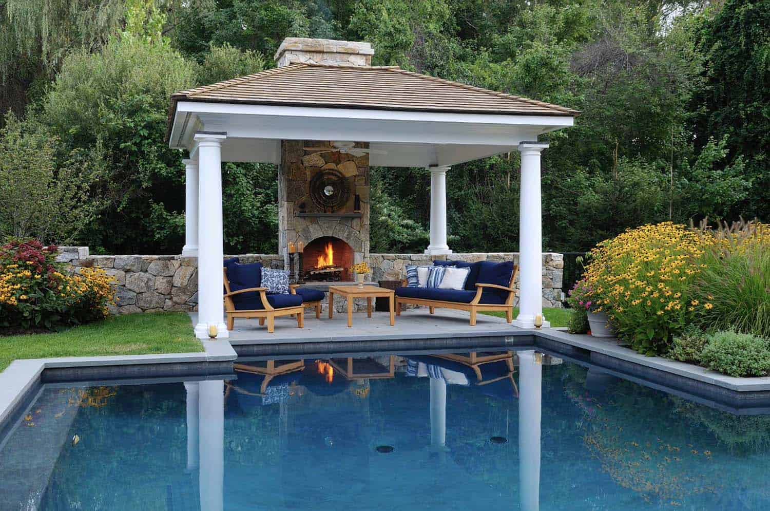 pergola covered outdoor living space with a fireplace next to a swimming pool