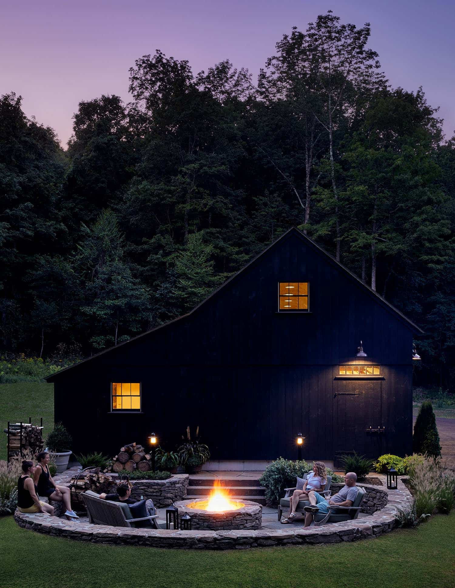 black barn garage exterior with a sunken outdoor living area and fire pit