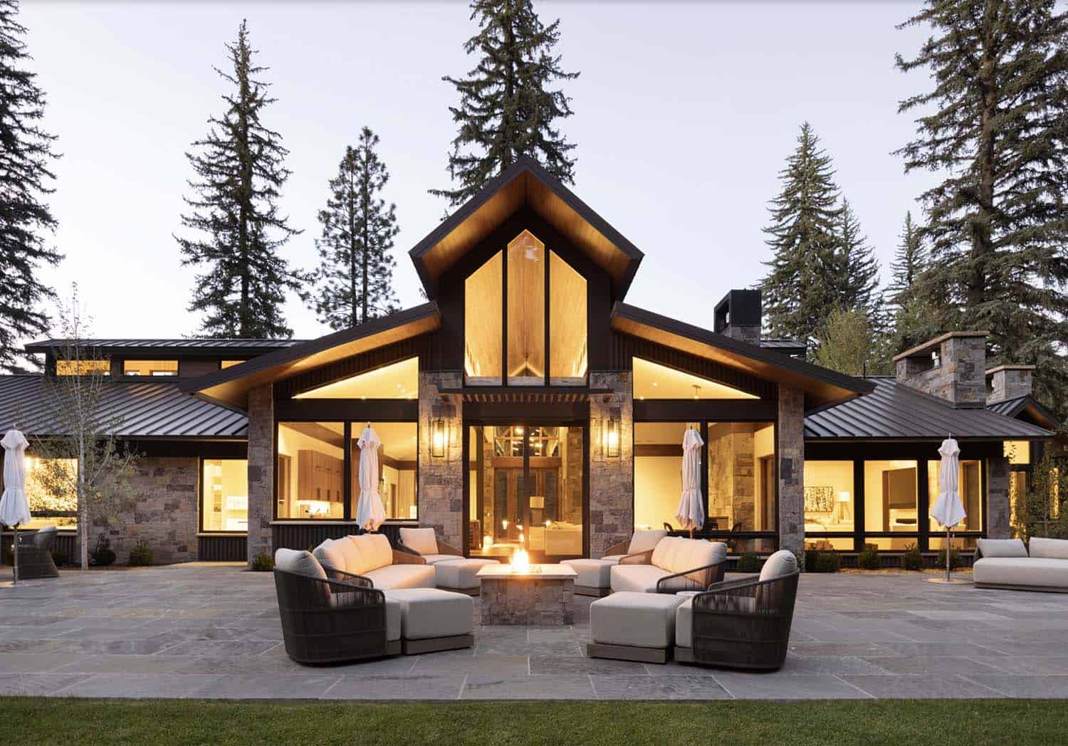 modern rustic mountain home exterior with a patio and a fire pit at dusk